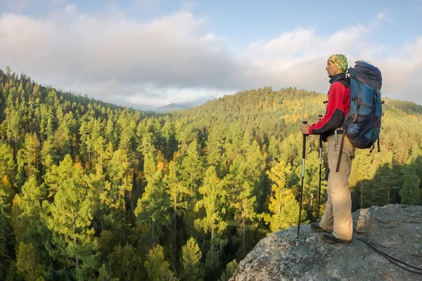 Hombre con mochila y bastón de trekking en bandana de pie sobre un roc — Foto de Stock