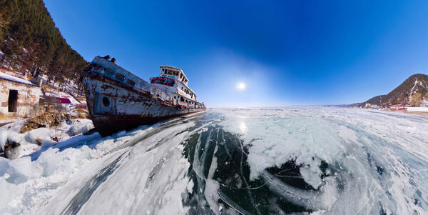 Old rusty ship on the coast of Lake Baikal among ice. Wide Panor