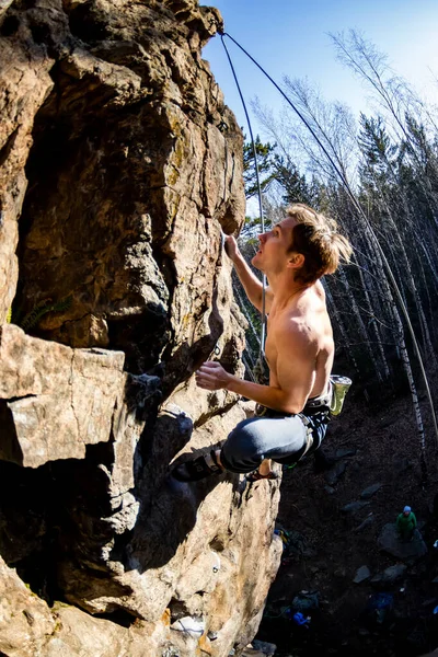 Escalador masculino com um tronco nu sobe em uma rocha com seguro superior — Fotografia de Stock