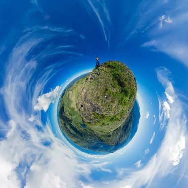 Landscape panorama lake in the shape of a heart among high green mountains and a male climber, on a sunny summer day and cloudy sky. Tiny little planet 360