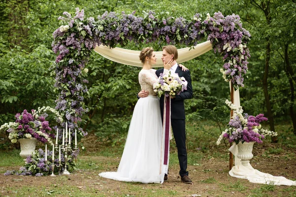 Nevěsta a ženich v blízkosti oblouku Lila v lese — Stock fotografie