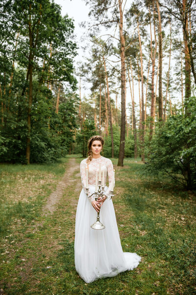 Girl in a beautiful white dress with a bouquet of flowers in the forest