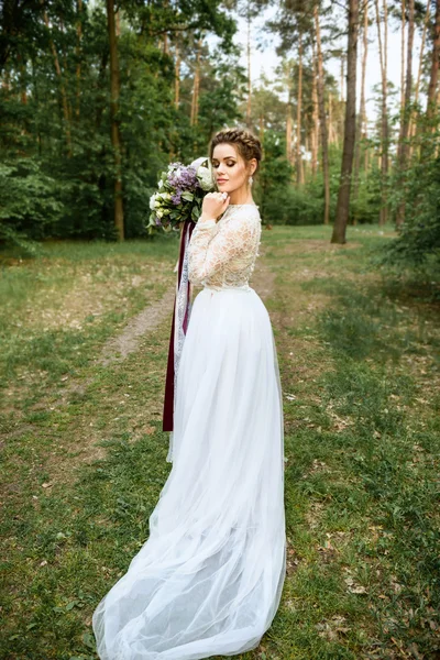 Chica en un hermoso vestido blanco con un ramo de flores en el bosque — Foto de Stock