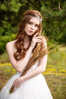 Kızıl saçlı genç kız ormanda. Parkta gelin portresi. Bir kız buğday kulakları elinde tutar. hippi kız