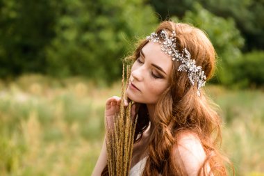 Kızıl saçlı genç kız ormanda. Parkta gelin portresi. Bir kız buğday kulakları elinde tutar. hippi kız