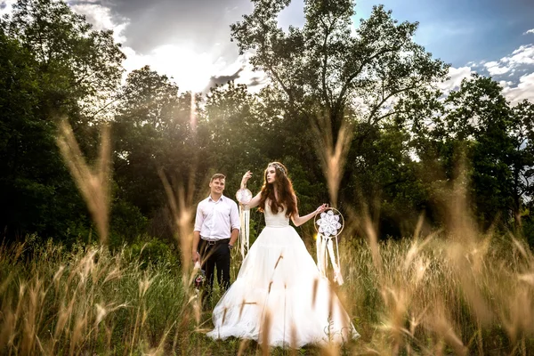 O casal nas orelhas de trigo na floresta. A noiva e o noivo nas orelhas de trigo no Parque. A noiva mantém em mãos charme — Fotografia de Stock