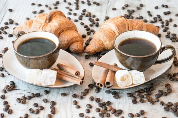 Cangkir kopi dengan biji-bijian, croissant, nikmat turkish dan tongkat kayu manis di latar belakang kayu — Stok Foto