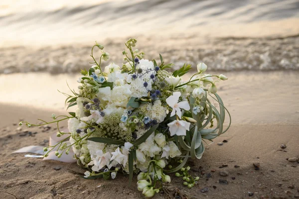 Bouquet de casamento na areia. Um buquê de flores deitadas na areia. Um buquê de flores perto da água ao pôr do sol — Fotografia de Stock