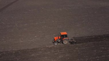 Ploughing red tractor at field cultivation work aerial view