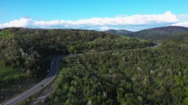 Uzun kamyonlar yol boyunca tırmanıyor, yokuş yukarı, dağlar ve ormanlar arasında, hava manzaralı.