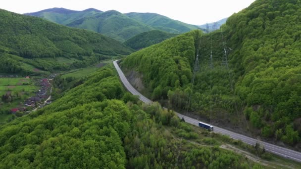 Truck rijden op de asfaltweg in een landelijk landschap met beboste bergen op de achtergrond luchtfoto — Stockvideo