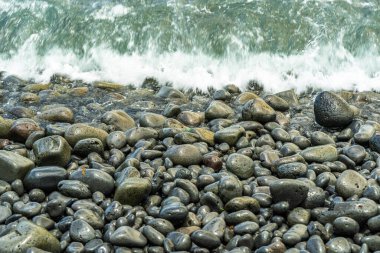 Wet round stones and pebbles of various sizes covering the entire beach surface, constantly washed by the tide. High quality photo
