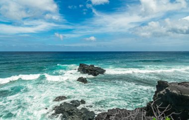 Dramatik kıyı manzarası: Bulutlu bir gökyüzü altında bazalt kaya oluşumlarının etrafından kırılan derin mavi okyanusun beyaz köpük dalgaları. Yüksek kalite fotoğraf