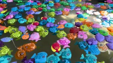 Gökkuşağı paleti yüzen oyuncak balık seti havuz suyunda yavaşça dönüyor rahatlatıcı ASMR dostane arkaplan görüntüsü oluşturuyor.