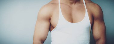 Tarafsız arka planda beyaz atlet giyen kaslı erkek gövdesinin yakın çekimi.