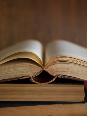 Open old book resting on stacked vintage books against wooden background