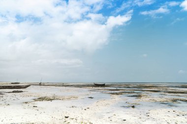 Parlak mavi gökyüzünün altında dağınık bulutlarla geniş kumlu kıyı şeridi