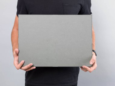 İki eli önde olan gri dikdörtgen bir nesne tutan genç bir erkek.