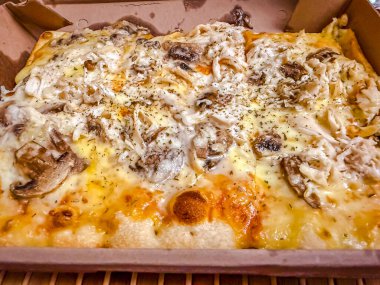 Karton kutuda erimiş peynirli dikdörtgen tavuk ve mantarlı pizza.