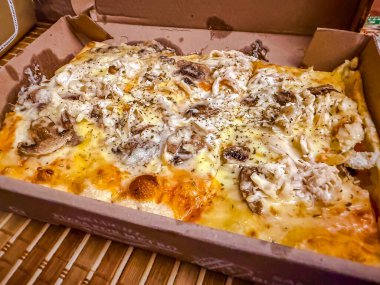 Karton kutuda erimiş peynirli dikdörtgen tavuk ve mantarlı pizza.