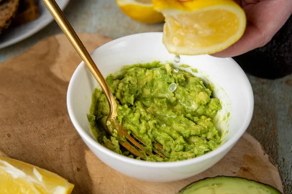Mashed avocado. Squeezing a lemon juice into plate with minced avocado