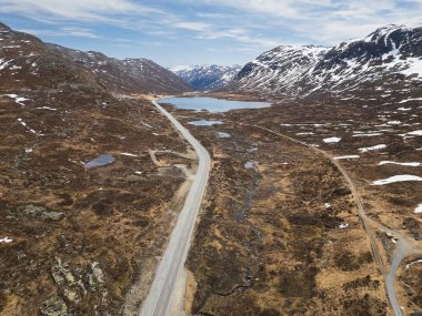 Norveç 'in görkemli dağ vadisinde, gölleri ve karla kaplı tepeleri olan manzaralı bir yolun insansız hava aracı görüntüsü..