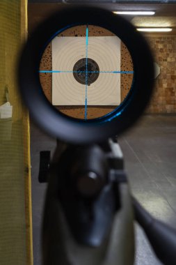 Kapalı alandaki bir atış poligonundaki kağıt hedefe doğrultulmuş mavi ışıklı bir parçayla tüfeğin dürbününden bak..