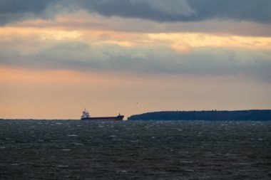 Endüstriyel bir yük gemisi fırtınalı Baltık Denizi 'nde Naissaar Adası, Estonya' da güzel, bulutlu bir günbatımına karşı yol alır..
