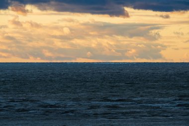 Altın bulutlarla dolu dramatik bir günbatımı gökyüzü Baltık Denizi 'nin karanlık, dalgalı ve huzursuz sularında asılı duruyor..