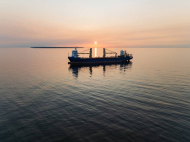 Baltık Denizi 'nde demirlemiş vinçleri olan büyük bir kargo gemisinin hava aracı görüntüsü. Güzel bir altın gün batımında..