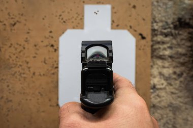 Birinci şahıs nişancının menzildeki bir kağıt hedefe kırmızı nokta görüşlü bir tabancaya nişan alması..