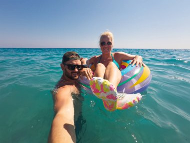 Adam renkli şişme halkalı bir kadınla çekim yapıyor, açık denizde güneşli bir yaz tatilinin tadını çıkarıyor..