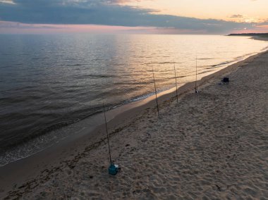 Estonya 'nın Perakula sahilinde, sakin Baltık Denizi üzerinde güzel bir günbatımında balık oltaları..