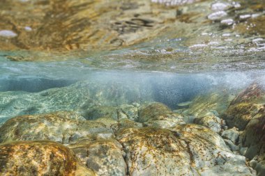Saint-Jean-Cap-Ferrat, Fransa 'da kayalık bir deniz yatağının ve çalkantılı su yüzeyinin iki katlı sualtı görüntüsü.