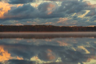 Tallinn, Estonya 'daki Harku Gölü' nün sakin ve sisli sularına yansıyan dramatik altın ve mavi bulutlar..
