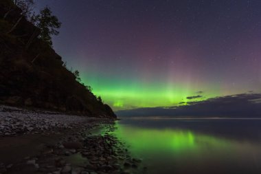 Sersemletici yeşil ve mor Aurora Borealis (Kuzey Işıkları) Estonya 'nın kayalık sahillerindeki sakin suları yansıtıyor.