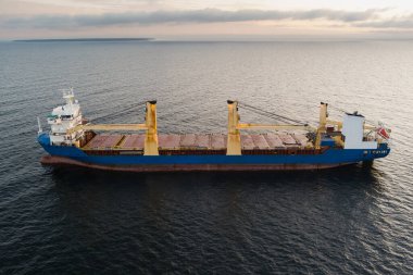 Gün batımında açık denizde yelken açan büyük mavi bir kargo gemisinin hava aracı görüntüsü..