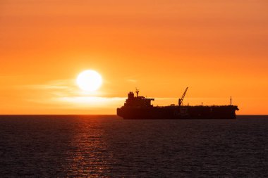 Estonya yakınlarındaki Baltık Denizi 'nde seyreden büyük bir kargo gemisinin silüeti dramatik bir altın turuncu gün batımı sırasında.