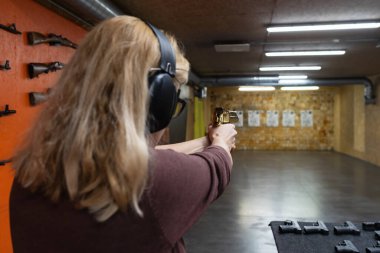 Sarışın kadının atış poligonunda kulaklık takarak altın tabancayla antrenman yaptığı arka görüş..