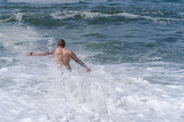 Güneşli bir günde Atlantik Okyanusu 'nun dalgaları arasında duran dövmeli bir adamın arka görüntüsü..