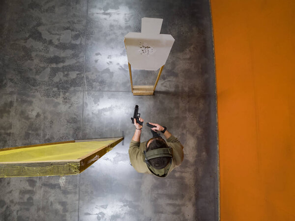 Вид сверху на человека, перезаряжающего пистолет на закрытом тире перед бумажной мишенью.