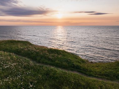 Saaremaa Adası 'nın dramatik yeşil kıyı kayalıklarından, Baltık Denizi üzerinde gün batımı Estonya' da huzurlu ve güzel bir doğal manzara sunuyor.. 