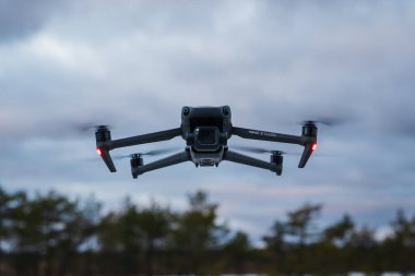 TALLINN, ESTONIA - 24 ARALIK 2025: DJI Mavic 3 Klasik İHA bulutlu bir kış gökyüzü ve ormana karşı havada süzülüyor.