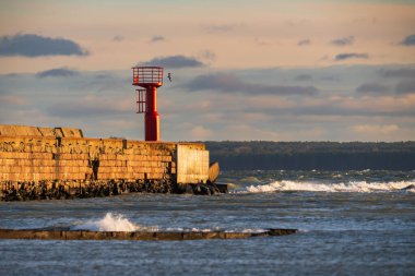 Tallinn, Estonya, Avrupa 'da gün batımında Baltık Denizi' nin dalgalanan dalgalarıyla dolu taştan bir iskelede kırmızı navigasyon feneri..