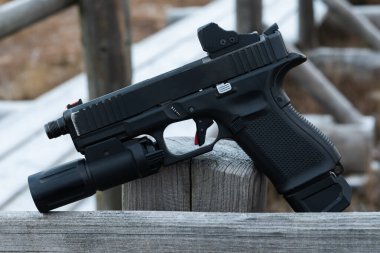 Modern yarı otomatik taktik tabanca. Kırmızı noktalı görüş ve el feneri eklentisi dışarıdaki ahşap çitin üzerinde duruyor..