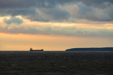 Kargo gemisi Baltık Denizi 'ne demir attı. Dalgalı dalgalarla birlikte dramatik bulutlu bir gökyüzünün altında, ormanlık bir adanın yakınında..