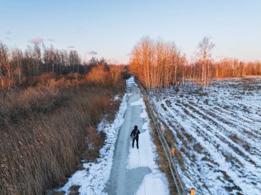 Altın bir kış günbatımı saatinde Estonya sulak alanlarında karlı bir yolda yürüyen yalnız bir yolcunun hava manzarası..