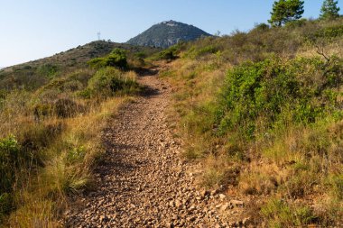 Fransa 'nın Nice kenti yakınlarındaki manzaralı Mont Chauve zirvesine giden dar kayalık yürüyüş yolu açık mavi gökyüzünün altında..