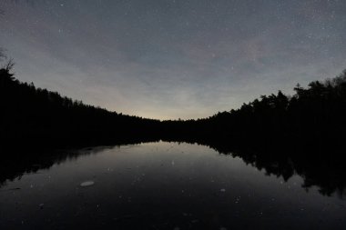 Donmuş Estonya gölünün göz kamaştırıcı gece manzarası kışın sessizliğinde karanlık ormanlarla çevrili yıldızlı bir gökyüzünü yansıtıyor..