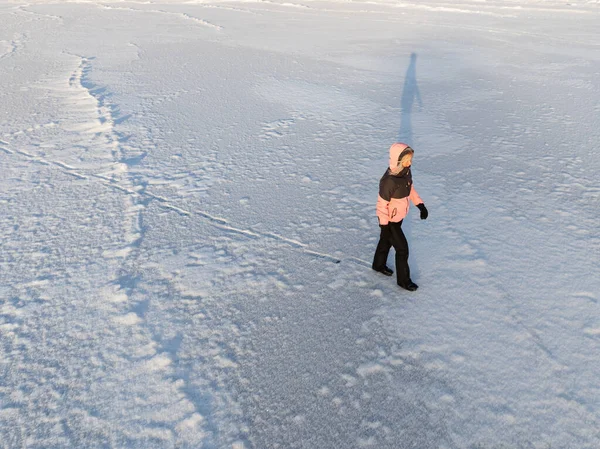 Yüksek açılı hava aracı, Estonya 'nın kış manzarasında donmuş bir göl yüzeyinde tek başına yürüyen bir kadının görüntüsü..